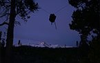Dark night sky over mountains with faint snow cover and a silhouetted object suspended between trees