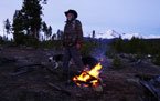 Person sitting near a campfire outdoors at night with mountains in the background