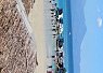 Crowded beach with many people relaxing under umbrellas along a coastline with mountains in the background