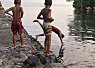 Children standing and balancing on rocks by a calm body of water during sunset