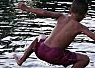 A young boy leaning forward while sitting on a wooden platform or pier above rippling water