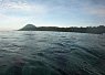 Calm equatorial sea with gentle waves under a clear sky, distant land with a low hill on the horizon