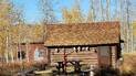 Rustic log cabin with animal skulls mounted on the wall, surrounded by autumn aspen trees with yellow leaves, a red water pump in front, and a wooden picnic table nearby