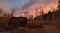 Small cabin surrounded by autumn aspen trees with a pink and purple sunset sky overhead