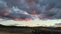 Sunset sky with dark clouds tinged with pink and orange over a forested landscape with distant snow-capped mountains