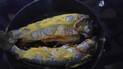 Two whole cooked fish in a pan with a yellow seasoning or sauce on top
