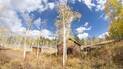 Rustic log cabin surrounded by yellow-leaved aspens under a blue sky with scattered clouds