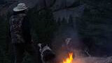 Person wearing a hat standing beside a small campfire on a rocky surface with two dogs, surrounded by forested mountains during dusk