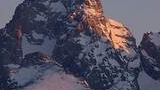 Mountain peaks covered in snow with the warm light of the setting or rising sun casting a pinkish glow on the rocky surfaces