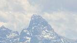 Snow-covered mountain peaks under a cloudy sky with a green grassy foreground