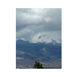 Snow-covered mountain peaks partially obscured by thick clouds above a forested valley