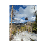 Backpack suspended on a wire between two trees in a snowy mountainous forest with partly cloudy blue sky