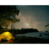 Glowing tent pitched near trees under a starry night sky with the Milky Way visible above a snow-covered hillside