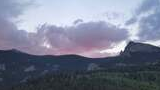 Mountain ridge with rock outcroppings and a forested valley under a twilight sky with pink and purple clouds