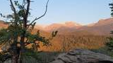 Sunlit mountain ridge with rocky outcroppings and pine trees in the foreground during early evening