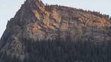 rocky mountain ridge with trees at the base illuminated by late sunlight