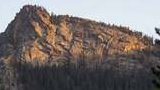 Rocky mountain ridge with patches of trees illuminated by warm sunlight against a clear sky