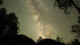 night sky filled with stars and the Milky Way galaxy above dark mountain silhouettes and trees