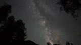 Star-filled night sky with the Milky Way galaxy visible above dark silhouetted mountain peaks and trees