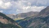 Mountain valley with dense pine forest and rocky peaks under a cloudy sky