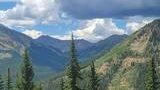 Mountain landscape with dense spruce and fir forests under a partly cloudy sky with dark rain clouds gathering