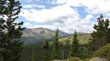 Green spruce trees and rocky outcroppings in a mountainous landscape under a partly cloudy blue sky