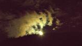 Bright full moon illuminating clouds above the silhouette of a forested mountain ridge at night