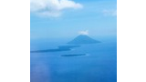 A distant view of a volcanic island rising from the blue sea under a partly cloudy sky