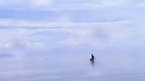 Person standing in shallow water surrounded by thick mist under a cloudy sky