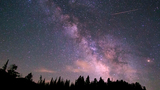 Starry night sky with the Milky Way visible above the silhouette of trees and a mountain ridge