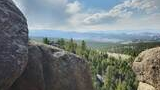 View through large granite boulders overlooking a forest of pine trees with distant mountain ranges under a partly cloudy sky