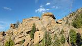 Large rounded rock formation with scattered pine trees and a bright blue sky with a few clouds