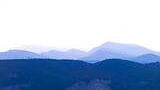 Layered mountain ridges fading into the distance under a pale sky, framed by tree branches on the sides