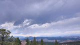 Cloudy sky over a forested mountainous landscape with pine trees and rocky outcroppings