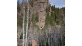 Large rocky outcropping surrounded by dense evergreen trees and leafless deciduous trees under a partly cloudy sky