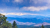 Snow-capped mountain range with layers of forested hills under a dramatic cloudy sky