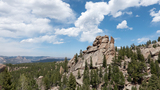 Rocky outcropping surrounded by dense pine forest under a partly cloudy blue sky