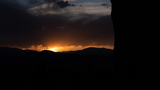 Early morning sunrise with dark clouds and silhouetted mountain range partially framed by a large rock formation on the right