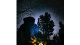 Illuminated tent nestled among trees and large rocks under a clear, star-filled night sky