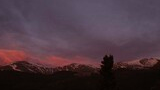 Mountain range with patches of snow under a dark sky with purple and pink clouds at dusk