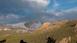 Silhouette of a dog standing on a rock formation with forested mountains and a partly cloudy sky in the background