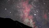 Silhouette of a mountain ridge under a vibrant night sky filled with stars and pinkish-red nebula clouds