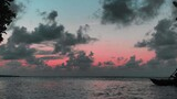Silhouetted person paddling a kayak on calm water at sunset with a sky of pink and blue hues and scattered dark clouds framed by tree branches