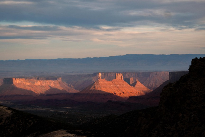 Sunlight illuminating red sandstone rock formations in a wide valley under a partly cloudy sky at sunset
