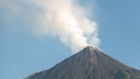 Volcano with dark slopes emitting a thick plume of white smoke against a clear blue sky