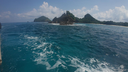 Turquoise ocean water with gentle waves approaching rocky, forested islands under a partly cloudy blue sky