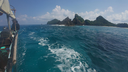 View from a small boat on clear blue ocean water headed toward rocky, forested islands under a partly cloudy sky