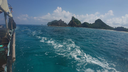 View from a boat looking toward small, rocky, and green-covered islands under a partly cloudy blue sky with clear turquoise ocean water around the boat