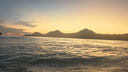 Golden light of sunset reflecting on gentle ocean waves with dark silhouette of mountainous island in the distance