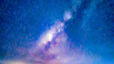 Night sky filled with stars and the Milky Way galaxy over dark silhouettes of islands and calm water reflecting some lights